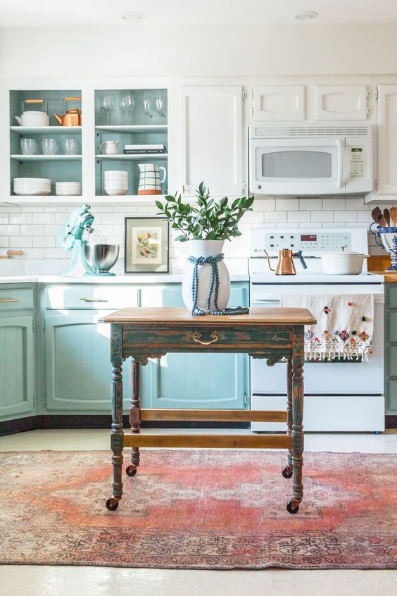 an eclectic kitchen with white and light blue cabinets, a white subway tile backsplash, open cabinets and a vintage table on casters