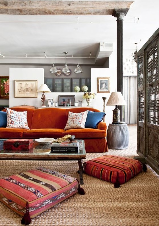 an eclectic living room with a burnt orange sofa, a low table and pretty tassel cushions and a table lamp