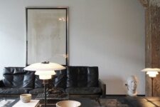 an eclectic living room with wabi-sabi beams and pillars, a black leather couch, a black coffee table and a daybed plus some lamps