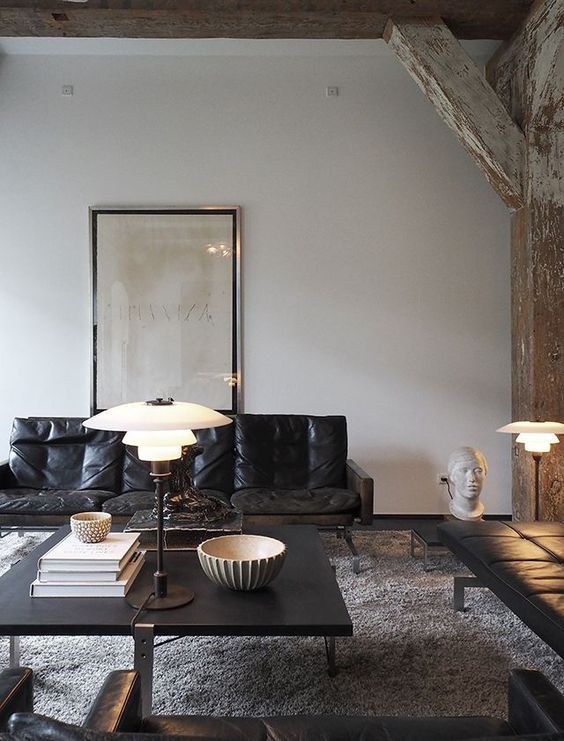 an eclectic living room with wabi-sabi beams and pillars, a black leather couch, a black coffee table and a daybed plus some lamps