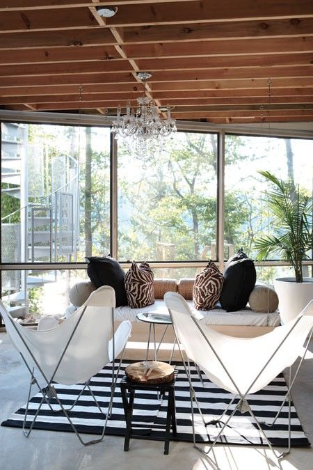 an eclectic sunroom with a glazed wall, a white sofa with printed chairs, white butterfly chairs, a small side table and a coffee table plus a striped rug