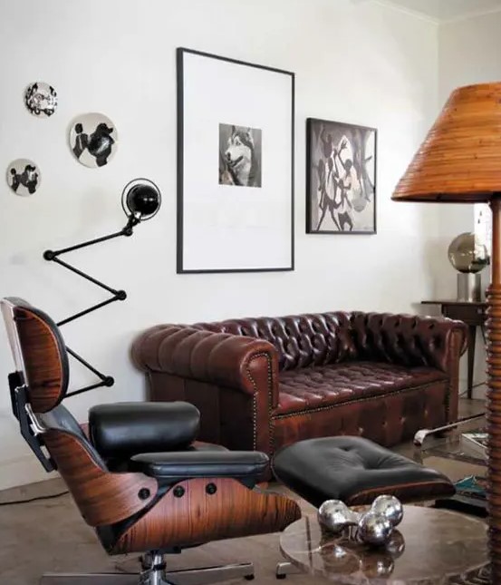 an elegant living room with a brown Chesterfield sofa, a black chair with a footrest, a side table, a black and white gallery wall