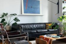 an elegant mid-century modern living room with a black leather sofa, black chairs, curved plywood furniture and a potted plant