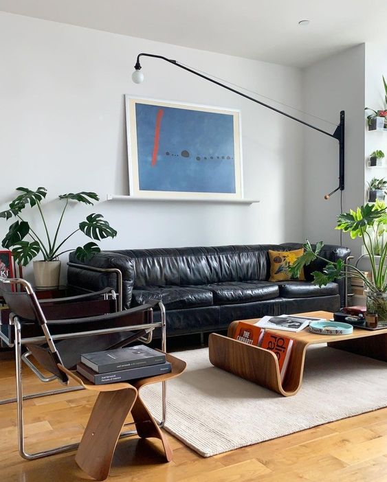 an elegant mid-century modern living room with a black leather sofa, black chairs, curved plywood furniture and a potted plant