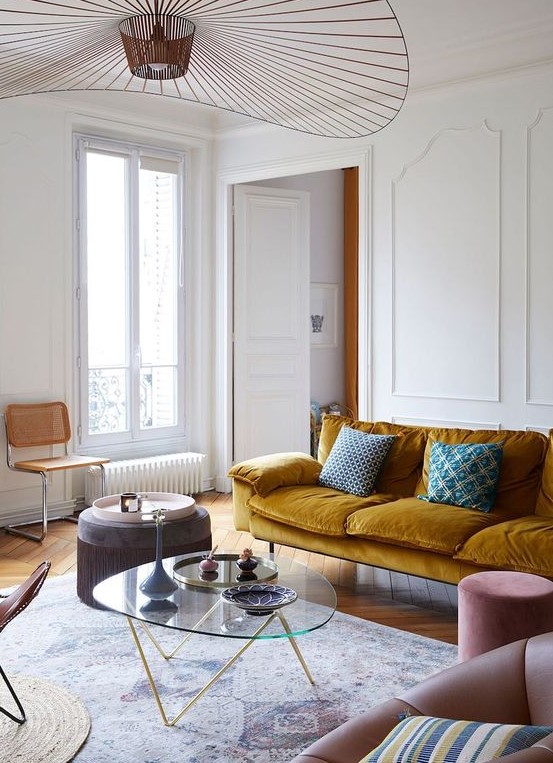 an exquisite Parisian living room with a mustard sofa, blush and brown chairs, a low glass table and a beautiful chandelier