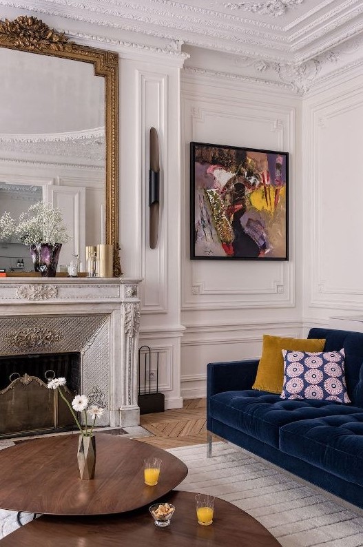 an exquisite living room with a French fireplace, a navy sofa with bold pillows, a bright artwork and layered coffee tables