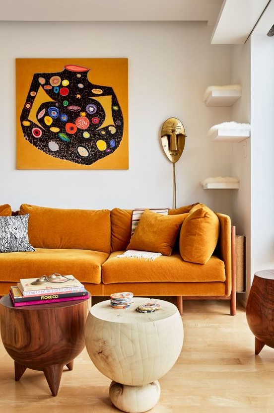 an exquisite living room with a honey yellow sofa, floating shelves for cats, round woodne tables and a bold artwork