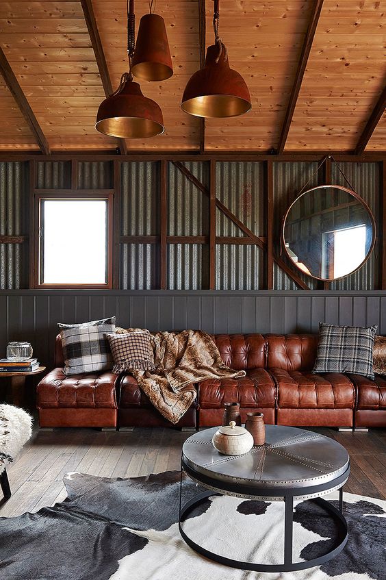 an industrial space with corrugated metal walls, a large rich brown sofa, a metal side table, printed pillows and copper pendant lamps