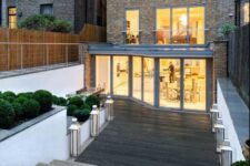 an outdoor space clad with charred and limed oak decking, with greenery in flower beds and lanterns that line up the pathway