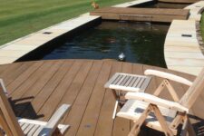 an outdoor space with coppered oak decking, folding wooden furniture, ponds with waterfall and fish and green grass