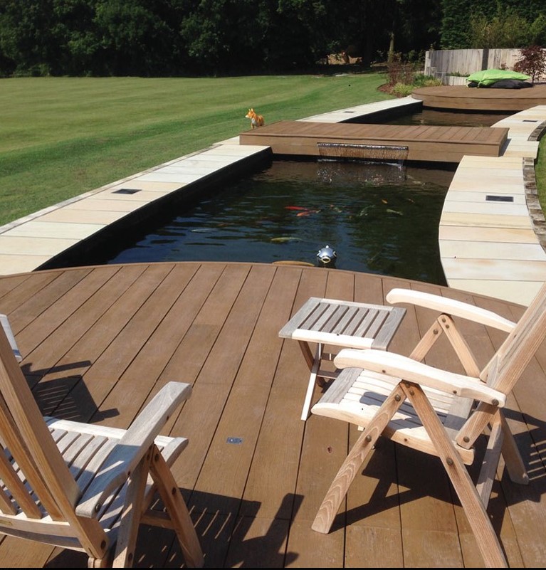 an outdoor space with coppered oak decking, folding wooden furniture, ponds with waterfall and fish and green grass