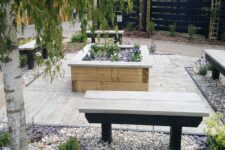 an outdoor space with weathered oak decking, benches, a flower bed with blooms, pebbles and trees