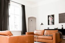 an ultra-modern and contrasting living room with two amber leather sofas, a printed rug, a coffee table, black curtains