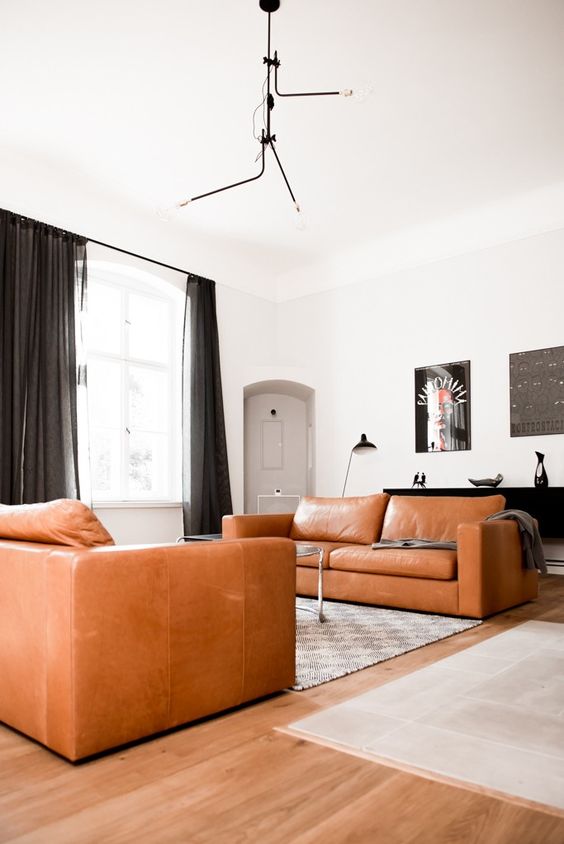 an ultra-modern and contrasting living room with two amber leather sofas, a printed rug, a coffee table, black curtains
