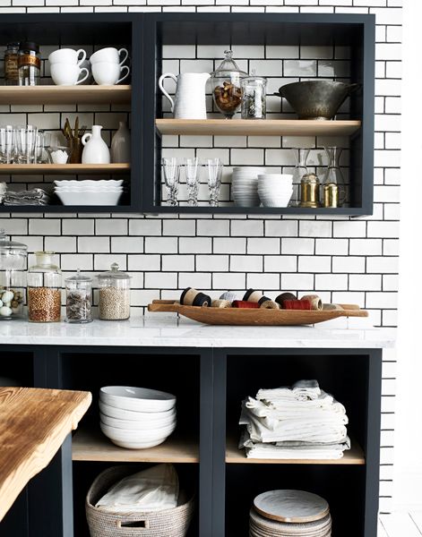 black open cabinets, a white subway tile backsplash and white countertops, stained shelves and beautiful tableware and dishes