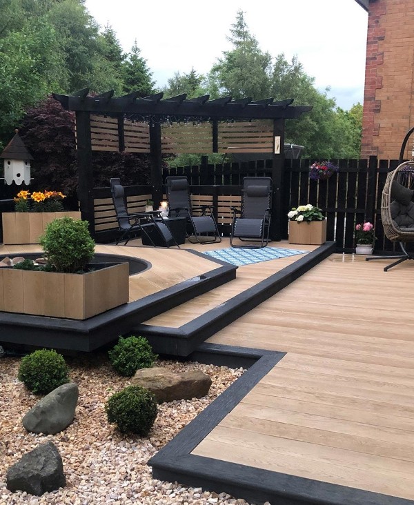 golden oak and burnt cedar millboard decking, a jacuzzi, black loungers, a side table and potted and growing plants