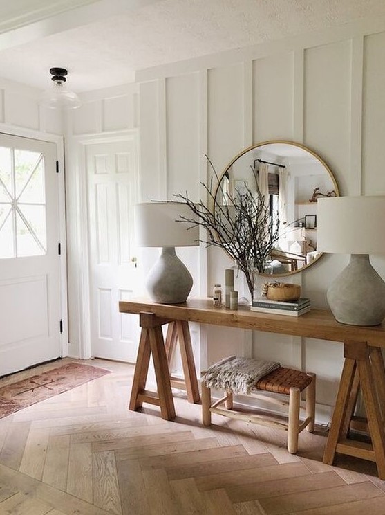 a farmhouse entryway with white paneled walls, wooden furniture, chic lamps and much natural light