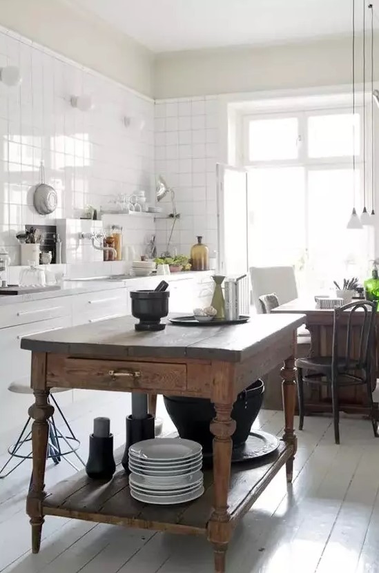 a white Scandinavian kitchen with white square tiles on the walls, a vintage stained kitchen island and a table in one, pendant lamps