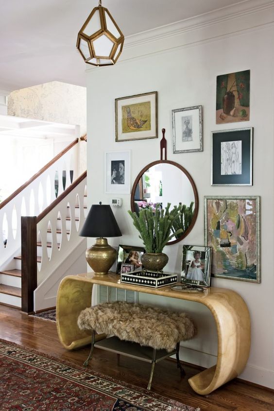 a whimsical entryway with a curved console table, a faux fur stool, a bright gallery wall with a mirror and some decor on the table