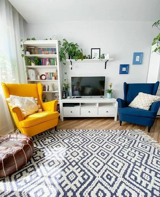 a Scandinavian living room with a bookcase, a TV unit, a navy and yellow Strandmon chair, a printed rug and a leather pouf plus potted greenery