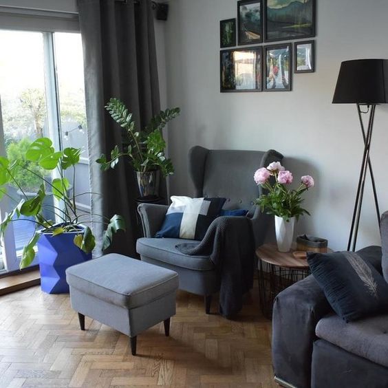 a Scandinavian living room with a grey Strandmon chair and an ottoman, a black sofa, potted plants, a black floor lamp and a gallery wall