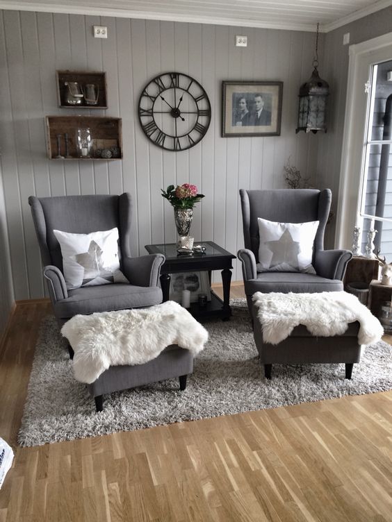 a Scandinavian sitting space with grey walls, box shelves, grey Strandmon chairs, ottomans, a grey rug and faux fur plus some decor