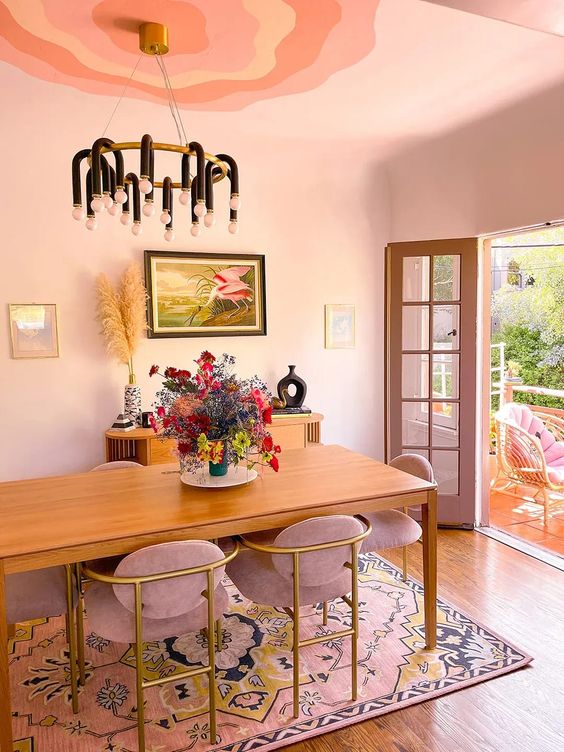  ديكورات غرفة طعام بألوان الباستيل A-blush-dining-space-with-a-stained-table-and-dusty-pink-chairs-a-pink-printed-rug-a-stained-credenza-a-black-chandelier
