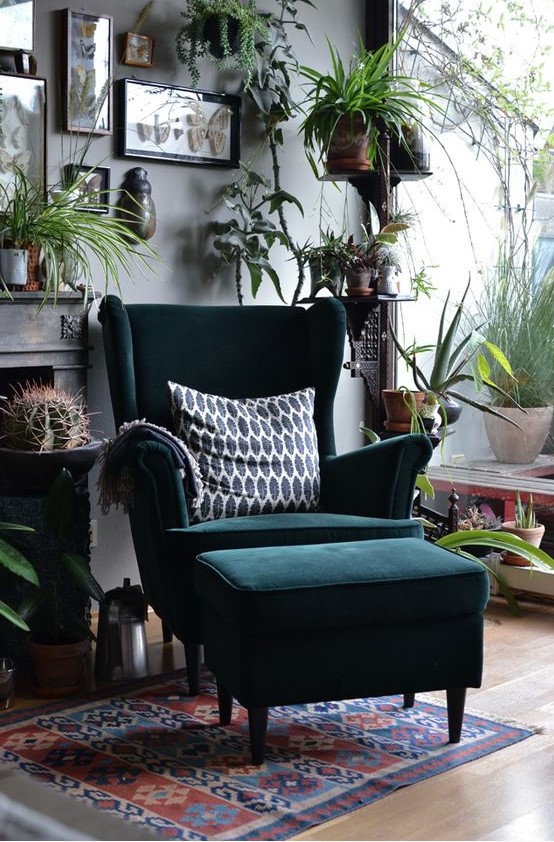 a bold boho nook with a dark green Strandmon wingback chair and a matching footrest, lots of greenery, cacti and artworks