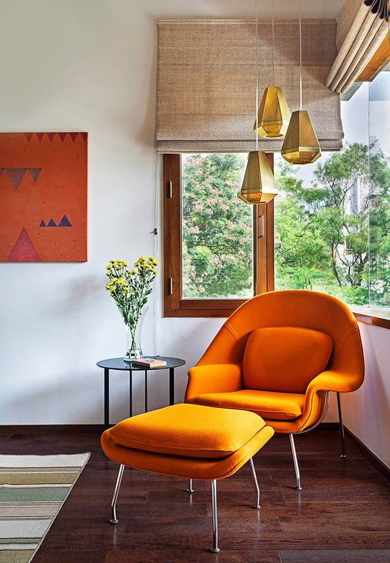 a bold corner window nook with an orange Wumb chair and ottoman, a side table, faceted pendant lamps and woven shades
