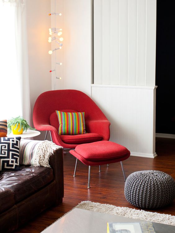 a catchy living room with a brown leather sofa, a red Wumb chair and ottoman, a grey knit pouf and a fluffy rug