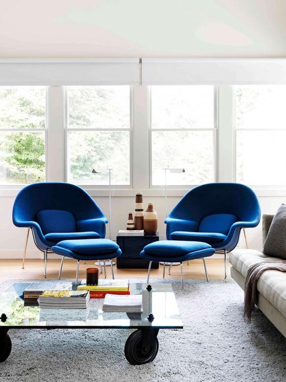 a catchy living room with a creamy sofa, blue Wumb chairs and ottomans, a glass coffee table on casters