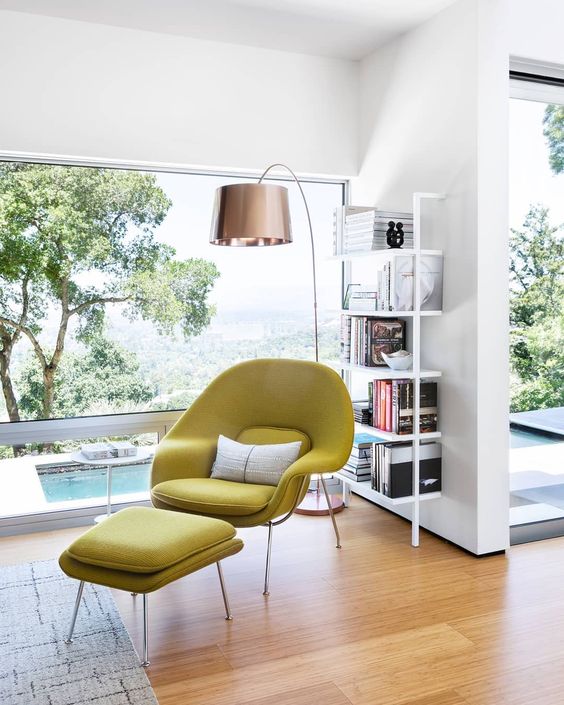 a catchy reading nook with a panoramic window, an airy bookshelf, a mustard Wumb chair and ottoman