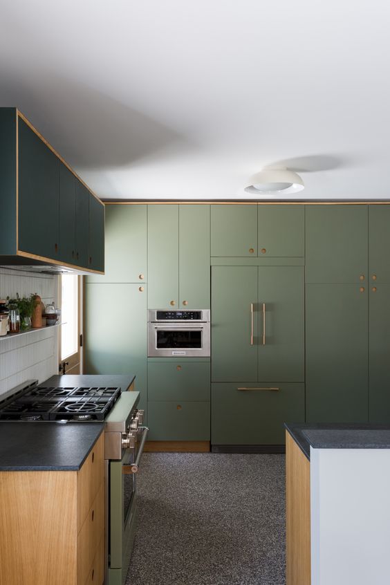 a chic olive green kitchen with flat panel cabinets, black countertops, a white tile backsplash and some gold touches