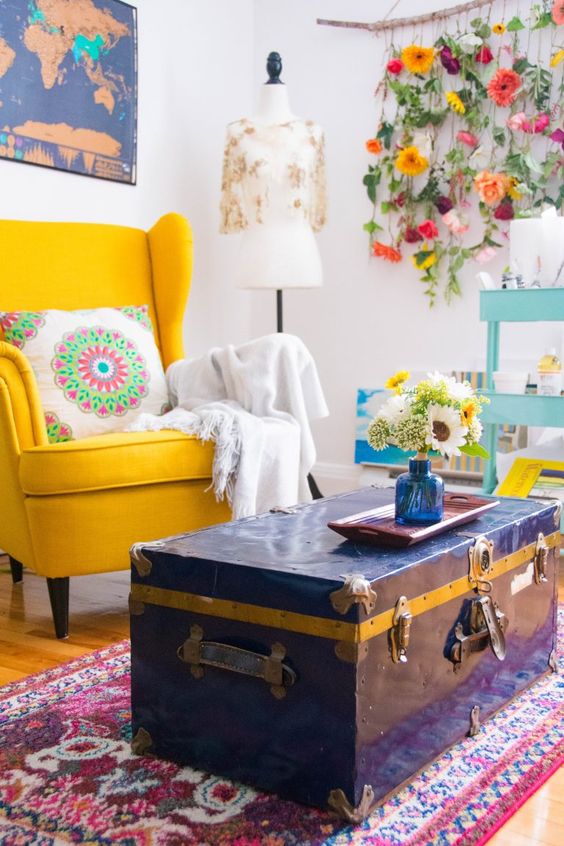 a colorful space with a yellow Strandmon, a navy chest as a coffee table, a printed rug, a floral decoration on the wall