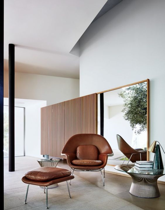 a contemporary space with a mirror in a frame, a brown leather Wumb chair and ottoman, a round coffee table and a table lamp