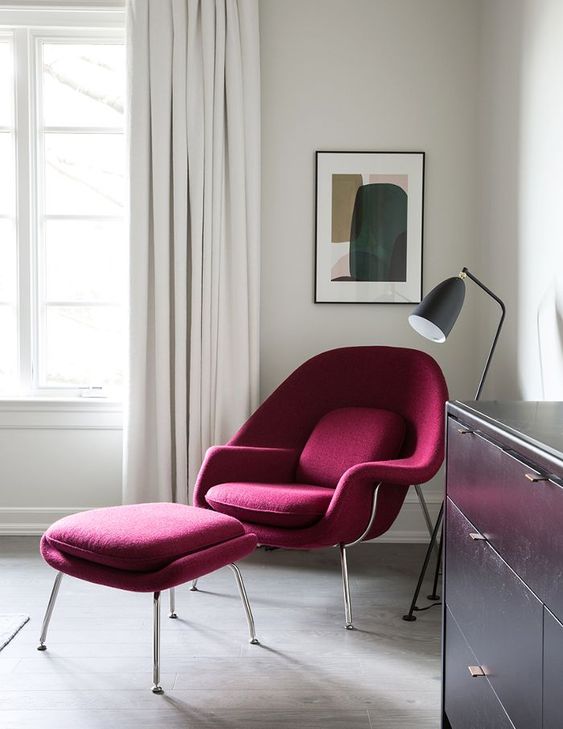 a contrasting nook with a burgundy Wumb chair and ottoman, a black floor lamp and a contrasting artwork, a black dresser
