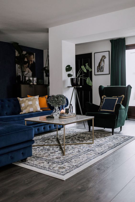 a cool living room wiht a navy sectional, a green Strandmon chair, a coffee table, a printed rug and some potted plants