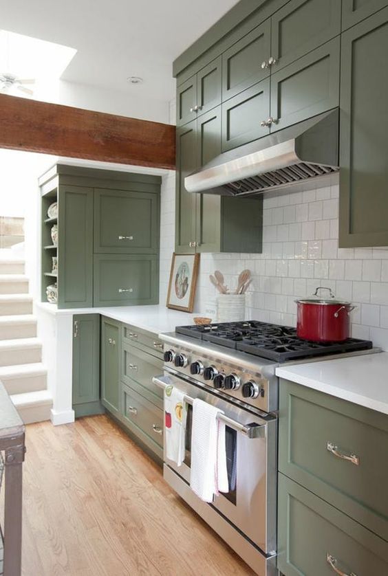 a cool olive green kitchen with shaker cabinets, a white square tile backsplash and white stone countertops, shiny knobs