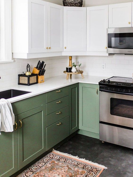 a cool two-tone kitchen with white and olive green shaker cabinets, white stone countertops and a white subway tile backsplash and gold knobs