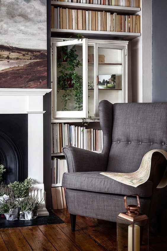 a cozy and welcoming living room with a fireplace, bookshelves, a cabinet with greenery, a grey Strandmon chair