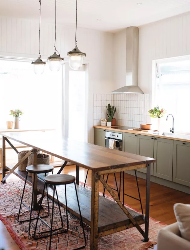 a cozy mid-century modern kitchen with lower olive green cabinets, a vintage wooden kitchen island, wooden stools and vintage pendant lamps