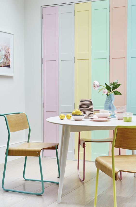 ديكورات غرفة طعام بألوان الباستيل A-fun-pastel-dining-space-with-bright-pastel-shutters-an-oval-table-plywood-chairs-pastel-tableware-and-some-blooms