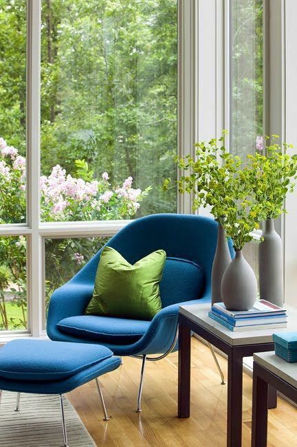 a glazed space with a blue Wumb chair and ottoman, side tables and greenery and books is amazing for reading here