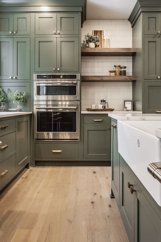 a large olive green farmhouse kitchen with shaker cabinets, white stone countertops, open shelves, a white subway tile backsplash