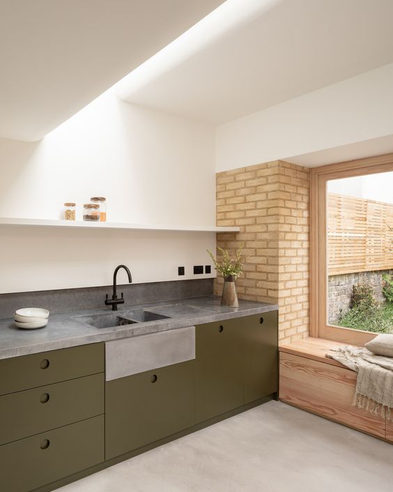 a minimalist olive green kitchen with sleek lower cabinets, grey stone countertops, an open shelf and a skylight over the space