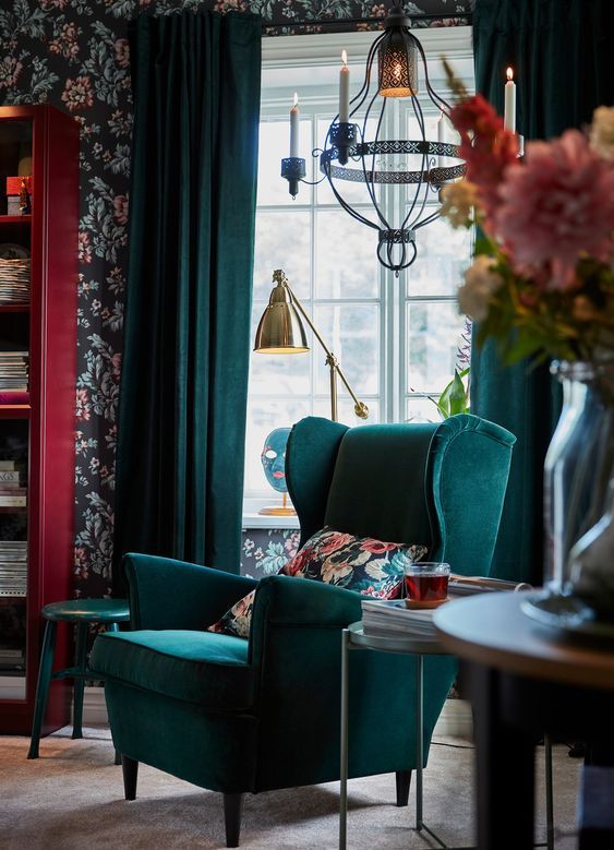 a moody and refined nook with some floral touches, a green Strandmon chair and a side table, a beautiful chandelier with candles