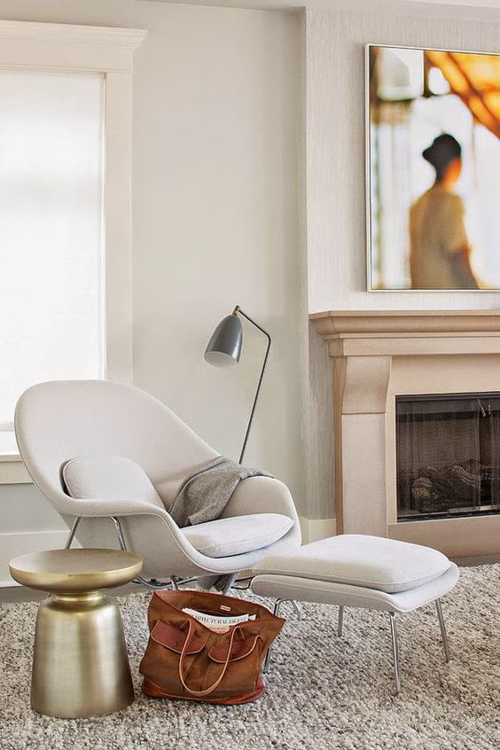a neutral space with a built-in fireplace, a neutral Wumb chair and ottoman, a polished metal side table and a floor lamp