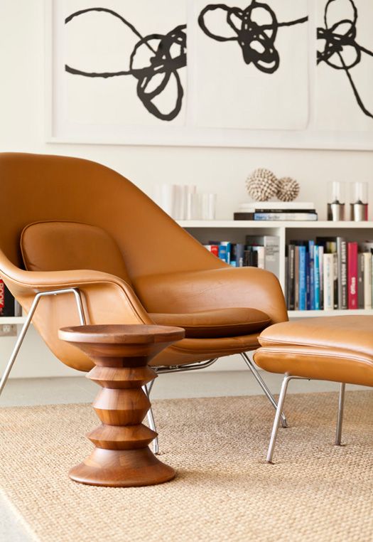 a refined space with a bookshelf, an amber leather Wumb chair and ottoman, a side table and abstract artwork