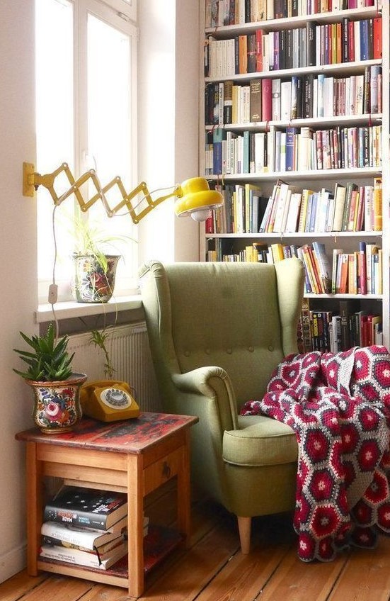 a retro cozy reading nook with a large bookcase, a green IKEA Strandmon wingback chair and a yellow wall lamp is very comfortable