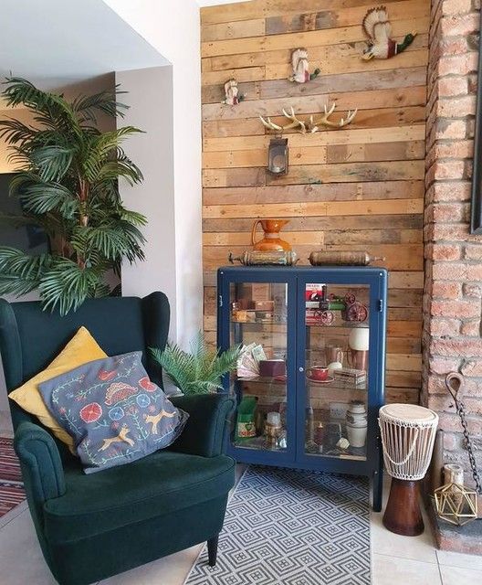 a rustic nook with a reclaimed wood wall, a blue buffet, a green Strandmon chair, printed pillows and a rug and antlers on the wall